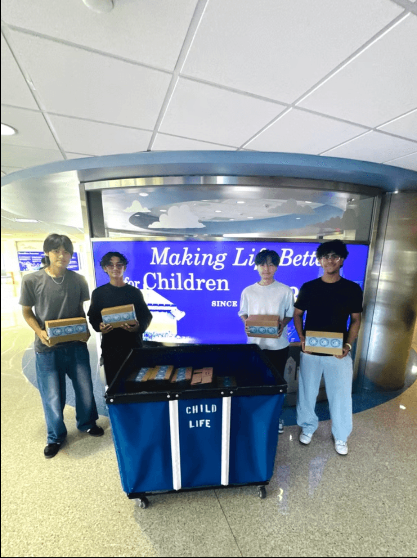 Four STEMSeeds members delivering kits beside a Child Life cart in a children's hospital