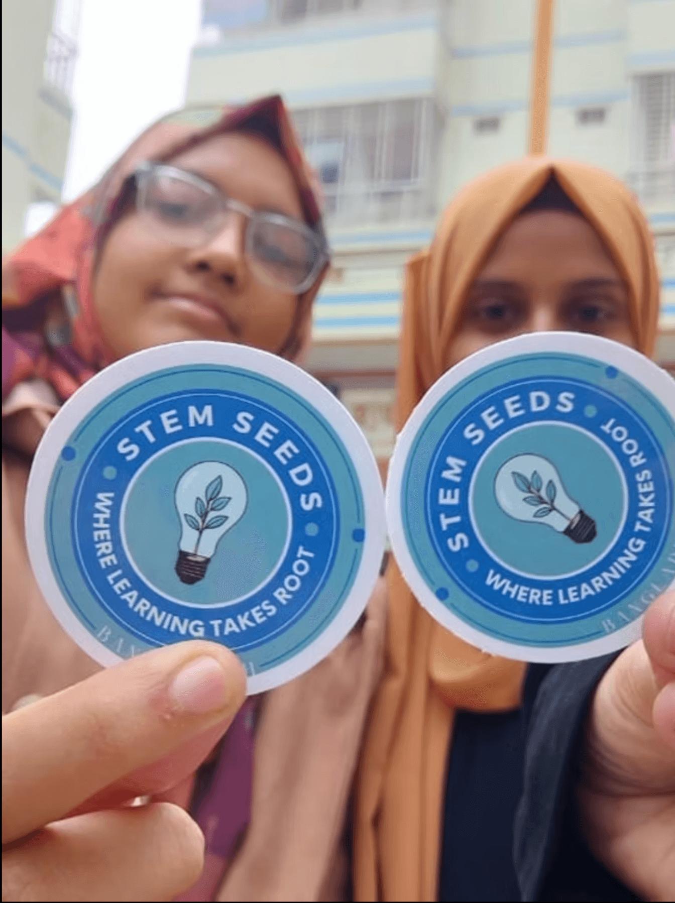 Two STEMSeeds chapter members in Bangladesh holding Where Learning Takes Root stickers
